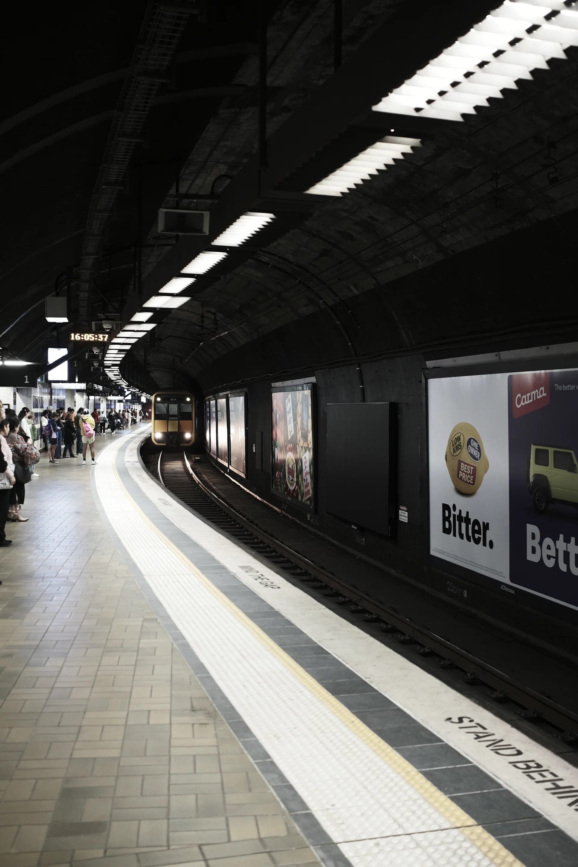 A train arriving at a curved underground platform beneath fluorescent lights.