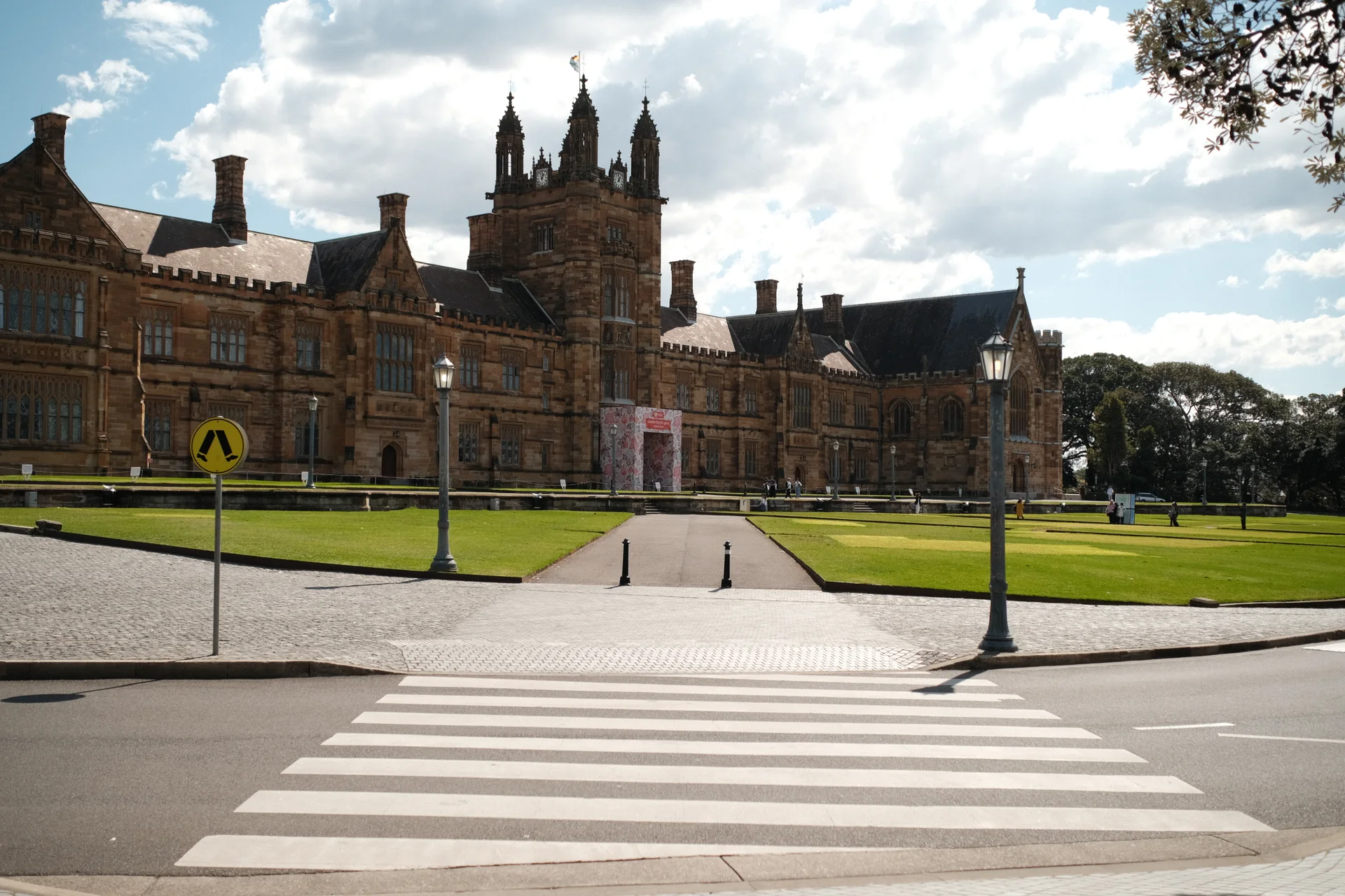 The University of Sydney's sandstone Quadrangle beneath a bright, cloud-filled sky.